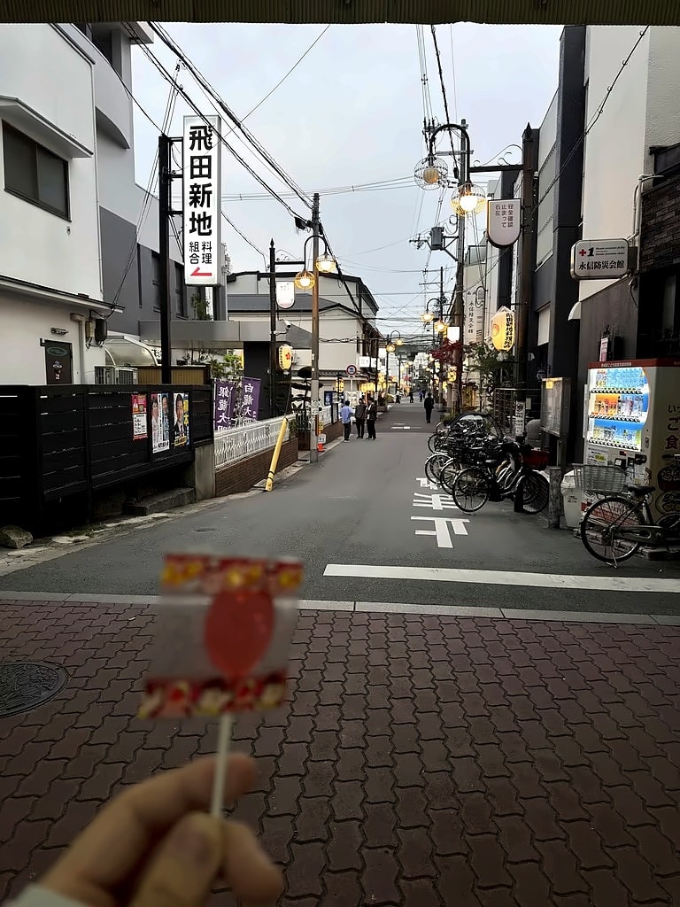 手持红色糖果望向傍晚亮灯的日本街巷