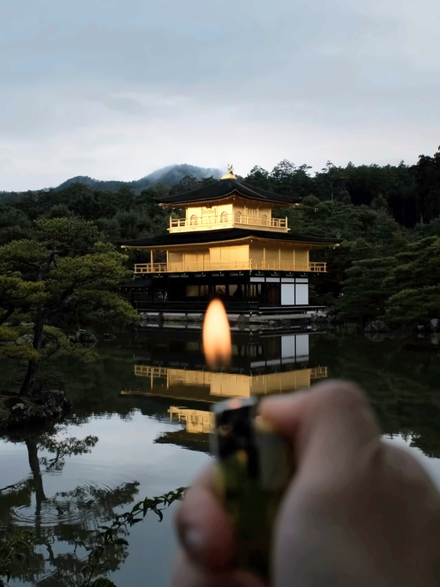 手持打火机点起火焰，对准池水中的金阁寺倒影