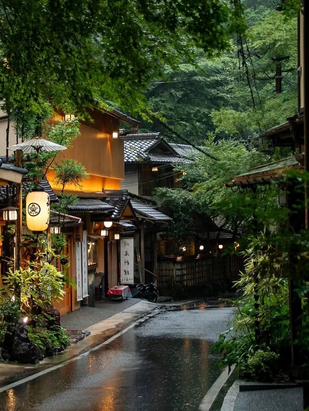 雨后京都街巷，灯笼暖光映湿路面，两侧日式木屋隐于翠绿。
