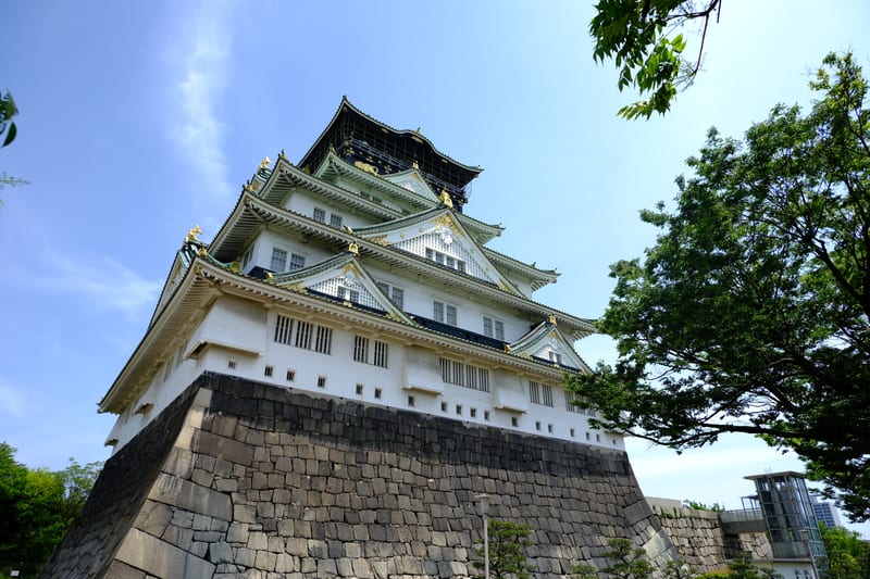 大阪城公园内白色城墙、金色兽头瓦与高耸石垣基座的天守阁仰拍